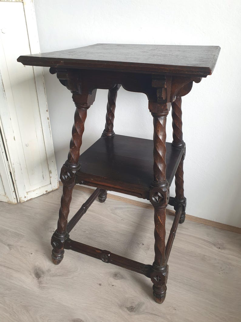 May include: Dark brown antique side table with a square top and a lower shelf. The table features intricately carved, twisted legs and decorative accents. The table's dimensions are approximately 24 inches tall, 18 inches wide, and 18 inches deep.