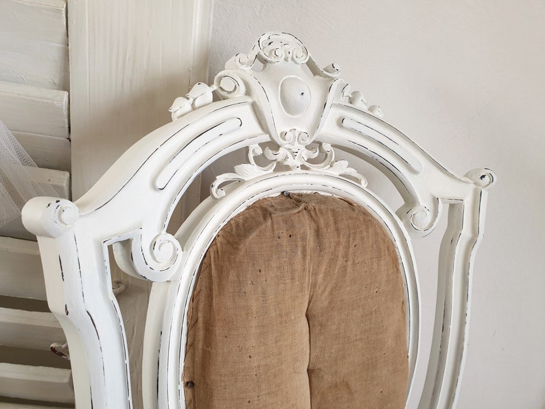 Puede incluir: Silla blanca pintada con un acabado desgastado y un asiento de tela marr&oacute;n. La silla tiene un dise&ntilde;o tallado y adornado.