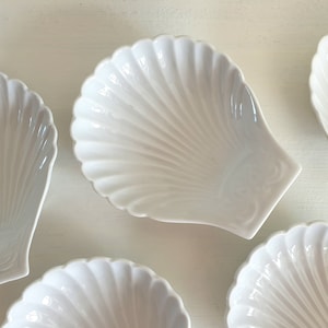 May include: Set of six white ceramic seashell-shaped bowls. The bowls are all the same size and shape, and they have a smooth, glossy finish.