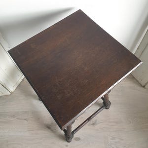 May include: A dark brown, square side table with a distressed finish. The table has four ornate legs and a connecting stretcher. The tabletop is approximately 24 inches square.
