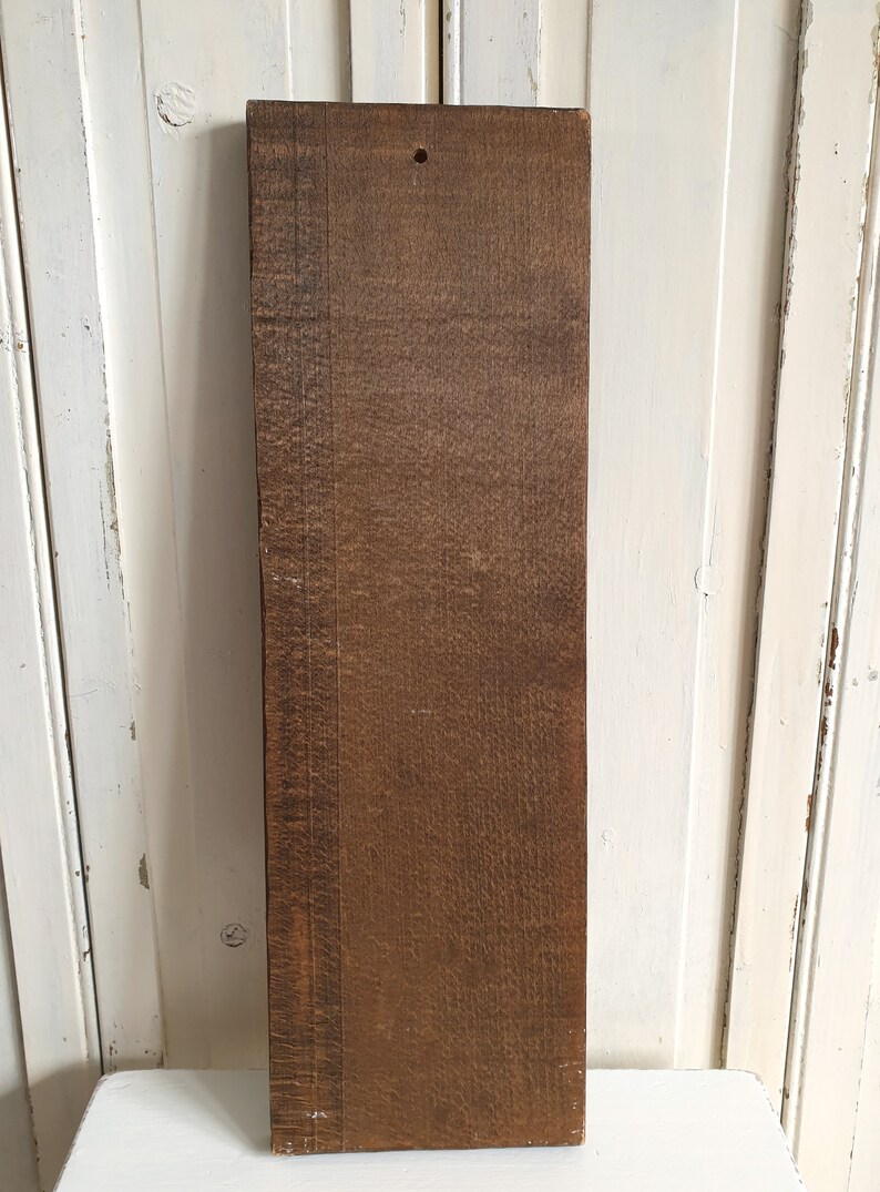 Puede incluir: Una tabla de madera rectangular con un color marr&oacute;n intenso y veta visible. La tabla tiene un agujero perforado cerca de la parte superior y mide aproximadamente 76 cm de largo. La madera parece envejecida y desgastada.