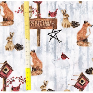 Op de afbeelding: Witte stof met een winterse bos-thema. De stof heeft rode kardinaals, vossen, eekhoorns, konijnen en dennenappels. De stof heeft ook een houten bord met de tekst "SNOW" met een ster die eraan hangt.
