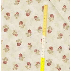 Può includere: Un tessuto beige con un motivo ripetuto di piccole rose rosse. Un righello giallo è posizionato sul tessuto, con i numeri da 0 a 21 visibili.