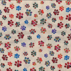 Puede incluir: Tela blanca con un patrón repetido de huellas de patas de colores. Las huellas de patas son de varios tonos de rojo, azul, verde y morado.