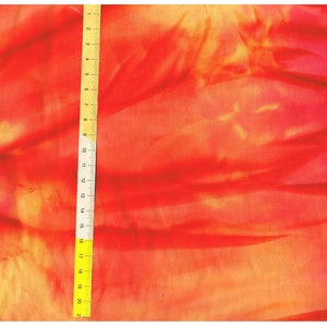 Pode incluir: Um close-up de um tecido vermelho e laranja com uma régua amarela medindo 53,3 cm. O tecido tem um padrão tie-dye.