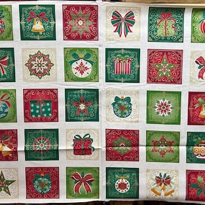 Op de afbeelding: Een wit katoenen stoffen paneel met een raster van vierkante blokken met kerstthema-illustraties, waaronder ingepakte cadeaus, ornamenten, strikken, sterren en hulst. De randen zijn afgewerkt met een verticaal hulstpatroon.