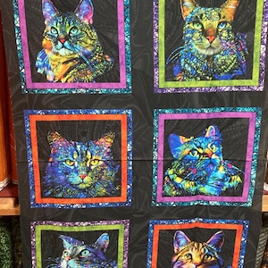 Peut inclure: Panneau de tissu avec six portraits de chats colorés dans des cadres carrés. Chaque chat a un design unique et vibrant sur fond noir. Les bordures supérieure et inférieure présentent un motif floral bleu et violet.
