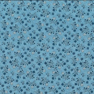 Può includere: Tessuto azzurro con motivo floreale. Il design presenta piccoli fiori stilizzati in tonalità di blu e bianco, disposti in un motivo ripetuto. Un righello giallo è posto sul lato destro del tessuto.