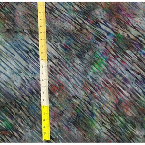 Pode incluir: Tecido abstrato com efeito aquarela. O tecido apresenta listras diagonais em tons de azul, verde, roxo e vermelho sobre um fundo cinza. Uma régua amarela é colocada verticalmente ao longo do tecido, mostrando medidas de até 50 cm.
