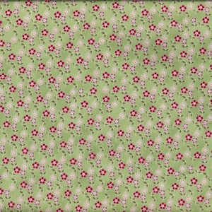 Op de afbeelding: Een lichtgroene stof met een herhalend bloemmotief. De bloemen zijn rood en wit, met kleine groene blaadjes. Een gele liniaal met zwarte markeringen staat rechts en toont afmetingen in centimeters.