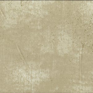 May include: Beige fabric with a distressed, textured finish. The fabric has a mottled effect with lighter patches and darker speckles. A yellow ruler with centimetre markings is visible along the right edge.