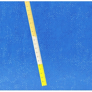 May include: A blue fabric with a white speckled pattern. A yellow ruler with black markings is placed diagonally across the fabric. The ruler is marked with numbers from 1 to 21.