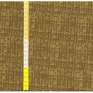 Op de afbeelding: Close-up van een stof met een gestructureerd, abstract patroon in tinten olijfgroen en bruin. Een gele liniaal met zwarte markeringen is verticaal langs de stof geplaatst en toont metingen in centimeters.