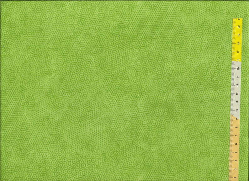 K&ouml;nnte beinhalten: Ein leuchtend gr&uuml;ner Stoff mit einem sich wiederholenden Muster aus kleinen, hellgr&uuml;nen Kreisen und Sechsecken. Ein gelbes Lineal mit schwarzen Markierungen befindet sich auf der rechten Seite und zeigt die Ma&szlig;e in Zentimetern an.