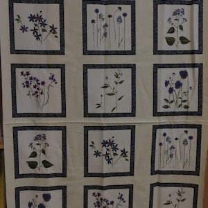 Pode incluir: Um tecido de cor creme com um padrão repetido de 12 desenhos florais emoldurados. Cada moldura é delineada em azul escuro e verde. Os desenhos florais apresentam flores roxas e verdes.