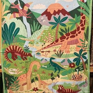 Op de afbeelding: Stofpaneel met een kleurrijke dinosaurusscène. Het ontwerp bevat verschillende dinosaurussen, vulkanen en palmbomen, met vliegende pterodactylen, een waterval en een rivier, alles tegen een blauwe lucht en groen landschap.