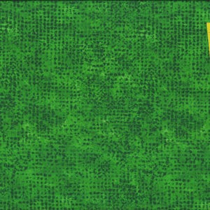 Op de afbeelding: Groene stof met een donkergroen stippenpatroon. Een gele liniaal is diagonaal over de stof geplaatst en toont metingen in centimeters. De stof heeft een getextureerd uiterlijk.