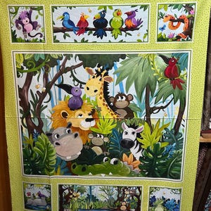 Op de afbeelding: Een rechthoekig stoffen paneel met een jungle-thema en een lichtgroene rand met stippen. De centrale illustratie toont een giraffe, leeuw, nijlpaard, aap, zebra en krokodil omringd door gebladerte, vogels en kleinere dieren in de hoeken.