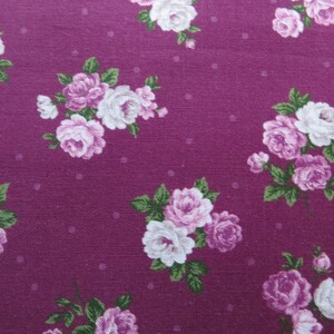 May include: A close-up of a purple fabric with a white and pink floral pattern. The fabric has a subtle polka dot pattern.