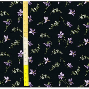 Puede incluir: Tela negra con un patrón repetido de pequeñas flores moradas y tallos verdes. La tela se mide con una regla en pulgadas.