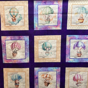 Może przedstawiać: Fioletowy materiał z powtarzającym się wzorem dziewięciu kwadratów. Każdy kwadrat zawiera akwarelową ilustrację balonu na gorące powietrze z innym zwierzęciem w środku. Zwierzęta obejmują niedźwiedzia, słonia, mysz, królika, pandę i kota. Tło każdego kwadratu jest jasnobeżowe z efektem akwareli.