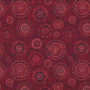 Op de afbeelding: Een close-up van een stof met een herhalend patroon van cirkelvormige ontwerpen in tinten rood en bordeaux. De cirkels hebben ingewikkelde patronen en zijn van verschillende groottes. Een gele liniaal staat aan de rechterkant van de stof en toont de afmetingen in centimeters.