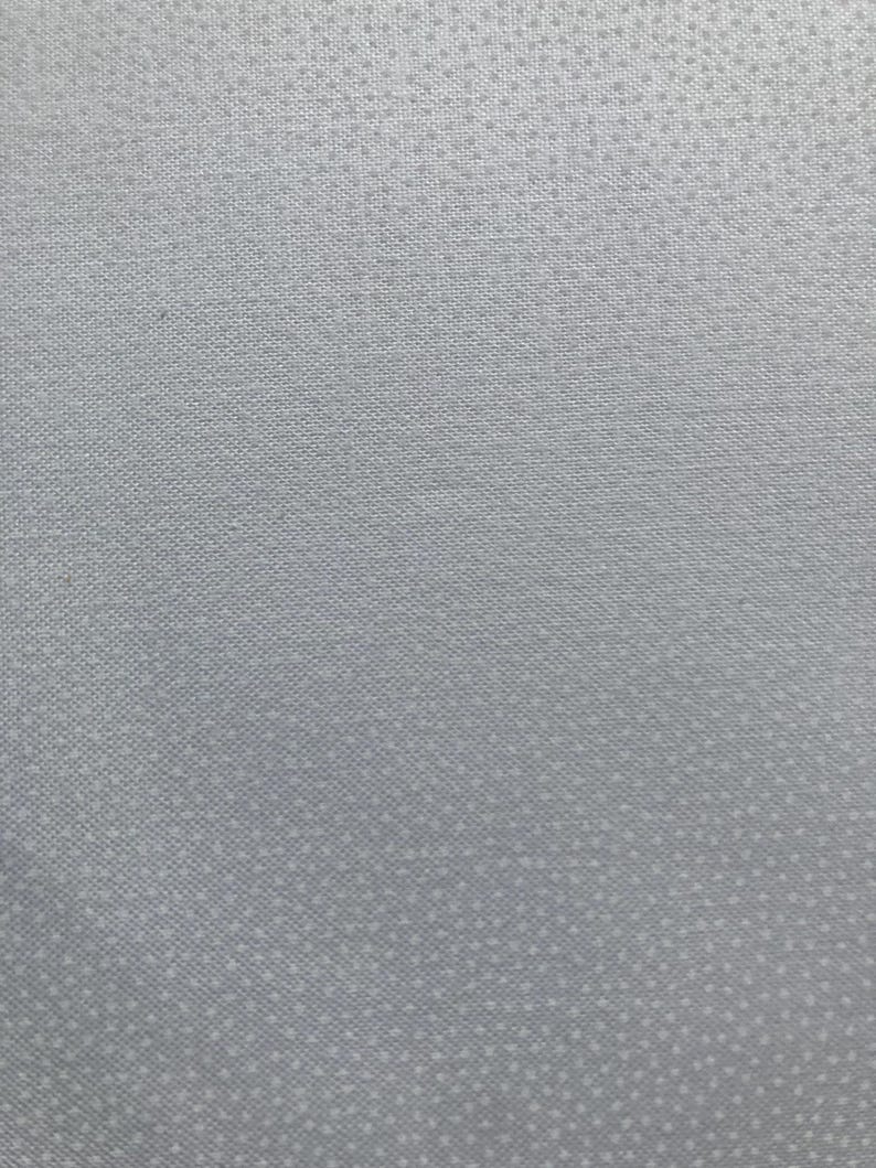 Pu&ograve; includere: Primo piano di un tessuto grigio chiaro con un motivo sottile e strutturato. Il tessuto ha un aspetto tessuto con piccoli punti distanziati uniformemente, creando una texture delicata e raffinata. Il tono generale &egrave; un grigio morbido e neutro.