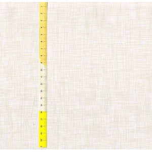 Op de afbeelding: Een close-up van een witte stof met een subtiele geweven textuur. Een gele liniaal is verticaal geplaatst aan de linkerkant van de afbeelding, met markeringen van 1 tot 21 inch (53,3 cm).
