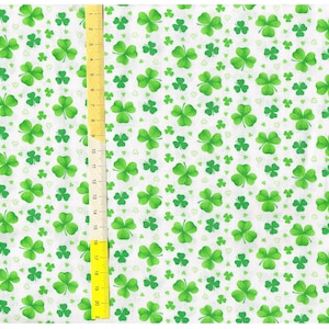 Puede incluir: Tela blanca con un patrón repetido de tréboles de cuatro hojas verdes. Una regla es visible en el lado derecho de la imagen.