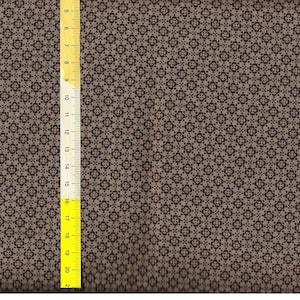 Könnte beinhalten: Ein brauner Stoff mit einem sich wiederholenden Muster aus kleinen schwarzen Quadraten und Kreisen.