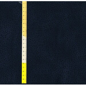 May include: A close-up of a dark blue fabric with a subtle textured pattern. A yellow measuring tape is visible on the left side of the image.