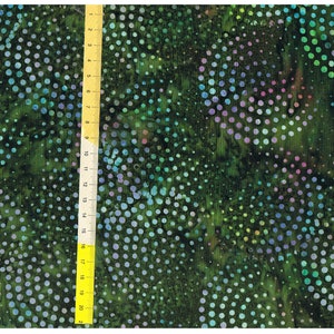 Pode incluir: Tecido verde com um padrão repetitivo de bolinhas iridescentes azuis, verdes e roxas. O tecido tem um design estilo batik com uma aparência manchada e texturizada.