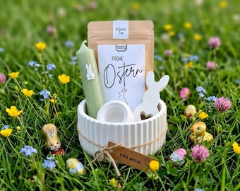 May include: A white ribbed ceramic bowl containing a light green candle with a white rabbit decal, a pouch of herbal tea labeled Frohe Ostern, and a white rabbit-shaped ornament. A brown paper tag tied with twine reads Für Dich.