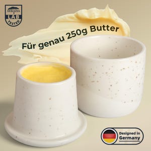 Pode incluir: Duas manteigueiras de cerâmica branca com design salpicado. Um prato contém manteiga amarela. O texto na imagem diz "Für genau 250g Butter" e "Designed in Germany". A imagem também inclui um logotipo "LAB TESTED".