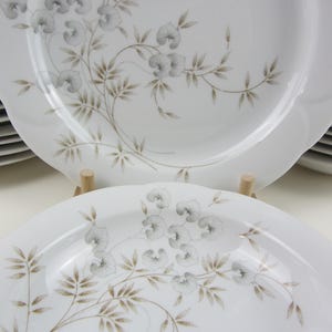 Könnte beinhalten: Ein Set weißer Keramik-Dinnerteller mit einem zarten Blumendesign mit grauen Blüten und braunen Blättern.