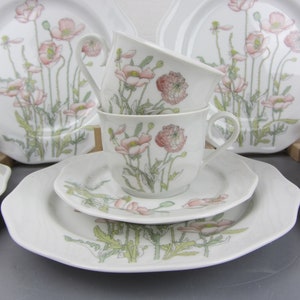May include: A set of white porcelain teacups and saucers with a floral design featuring pink poppies and green leaves.