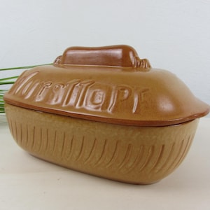 Könnte beinhalten: Eine braune Keramik-Auflaufform mit Deckel. Die Form hat eine rechteckige Form mit vertikalen Rillen an den Seiten. Auf dem Deckel steht der Schriftzug "Wurttember". Die Farbe ist ein warmer, erdiger Ton.