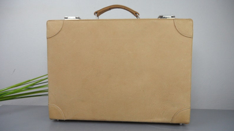 Pu&ograve; includere: Una valigia in pelle marrone con maniglia in pelle marrone e accessori argentati.
