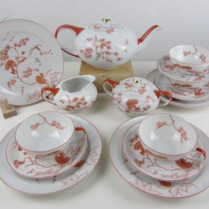 以下が含まれることがあります： 赤と茶色のリスと花柄の白い磁器製のティーセット。ティーポット、クリーマー、シュガーボウル、ティーカップ2個、ソーサー2個が含まれています。