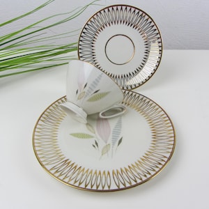 Può includere: Un servizio da tè vintage composto da tazza, piattino e piatto. I pezzi in porcellana bianca presentano bordi dorati e un delicato motivo floreale rosa, verde e grigio. Ideale per servire tè o caffè.