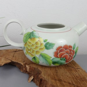 May include: White porcelain teapot with a floral design. The teapot has a red rim and features yellow and orange flowers with green leaves.