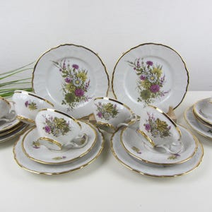 May include: A vintage tea set featuring white porcelain cups, saucers, and plates with a gold trim. Each piece is decorated with a floral design in shades of yellow, purple, and green. The set includes teacups, saucers, and plates.
