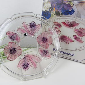 May include: A clear glass cake plate with a raised edge and a floral design. The plate features pink and purple flowers with a textured, embossed look. The plate is labeled "Renaissance" and "Plat à tarte".