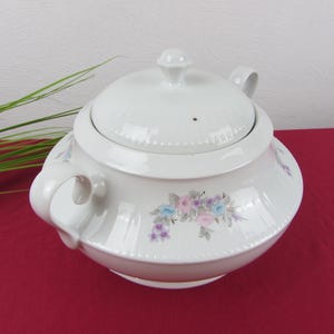 Peut inclure: Une soupière en céramique blanche avec couvercle assorti, dotée de deux anses latérales et d'un motif floral composé de fleurs roses, bleues et violettes avec des feuilles grises. Le couvercle possède un bouton central et une petite évacuation.