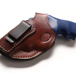 May include: A brown leather holster with a black clip for a blue handgun.