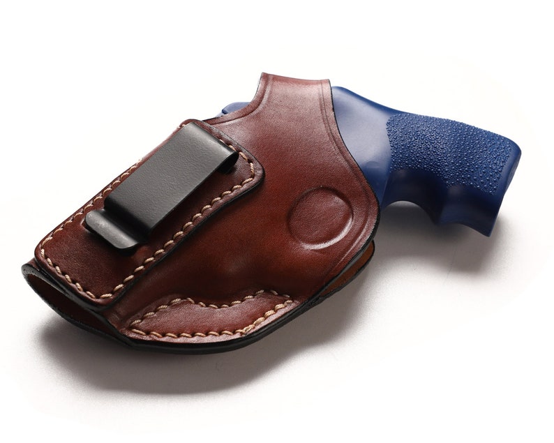 May include: A brown leather holster with a black clip for a blue handgun.
