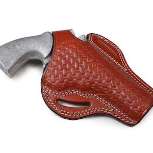May include: A brown leather holster with a woven pattern and white stitching. The holster is designed to hold a handgun.