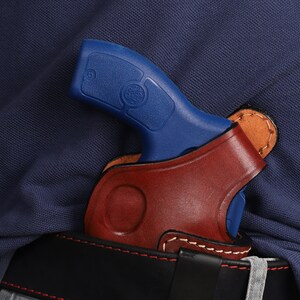 May include: A blue handgun with a brown leather holster. The holster is attached to a black belt.