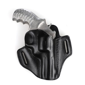 Op de afbeelding: Een zwart leren holster voor een zilveren revolver. Het holster heeft een riemlus en een drukknopsluiting.