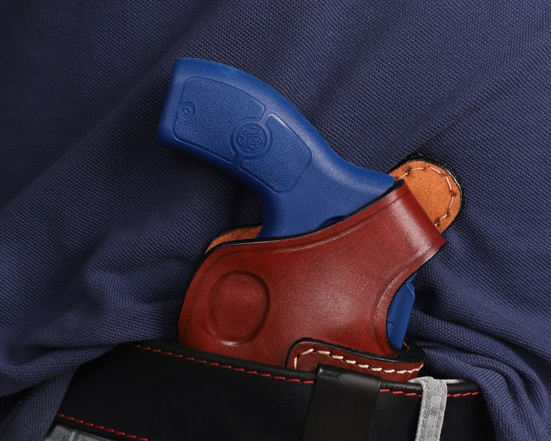 Puede incluir: Una pistola azul con una funda de cuero marr&oacute;n. La funda est&aacute; unida a un cintur&oacute;n negro.